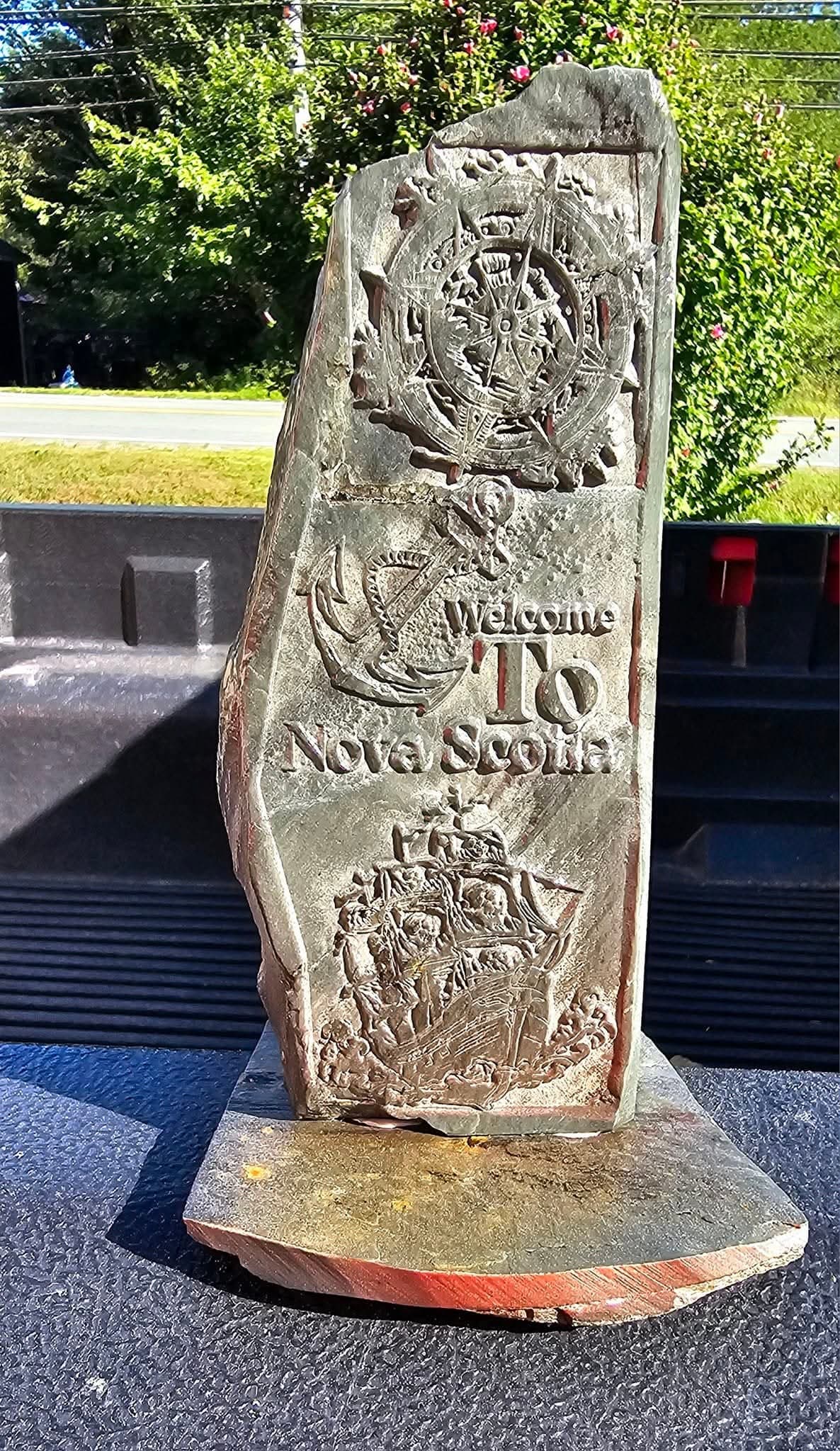 Hand-carved "Welcome to Nova Scotia" stone — compass, anchor, and ship carvings on natural rock, mounted on a wood base